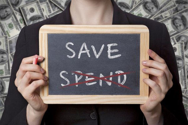 Hands holding a small chalkboard with the words Spend and Save, with Spend crossed out.